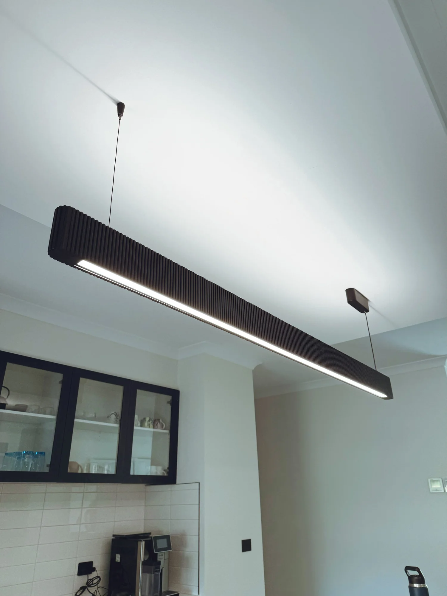 Modern rectangular black pendant light fixture hanging from the ceiling over a kitchen area.